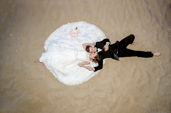Beach wedding photo, bride and groom on the beach, laying on the sand,